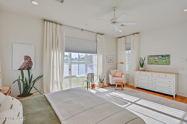 bedroom with hardwood / wood-style floors, a water view, and ceiling fan