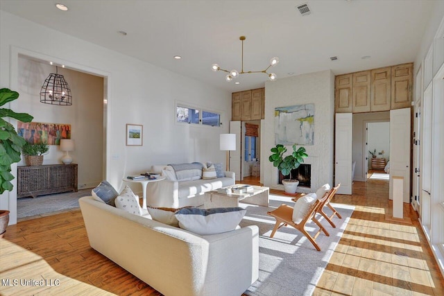 living room with a large fireplace, a notable chandelier, and light hardwood / wood-style flooring