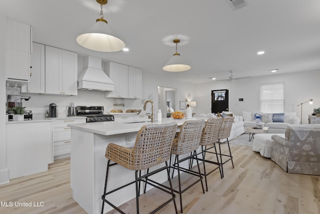 kitchen featuring stainless steel stove, a sink, open floor plan, light countertops, and custom exhaust hood