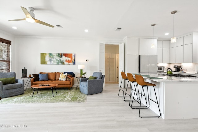 living room featuring light wood-type flooring, ceiling fan, visible vents, and crown molding