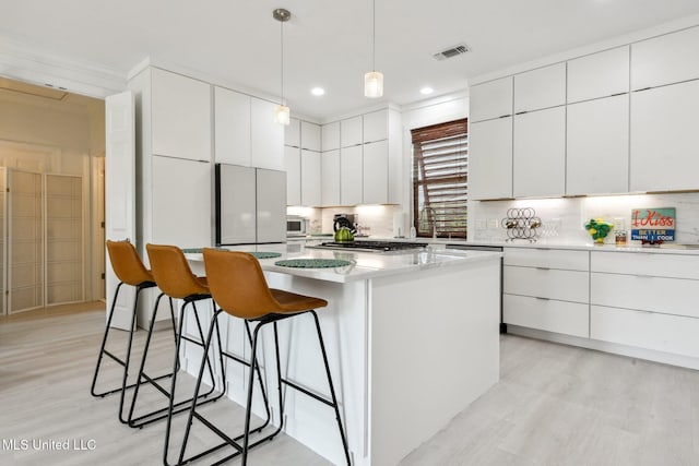 kitchen with a kitchen island, visible vents, a kitchen breakfast bar, freestanding refrigerator, and modern cabinets