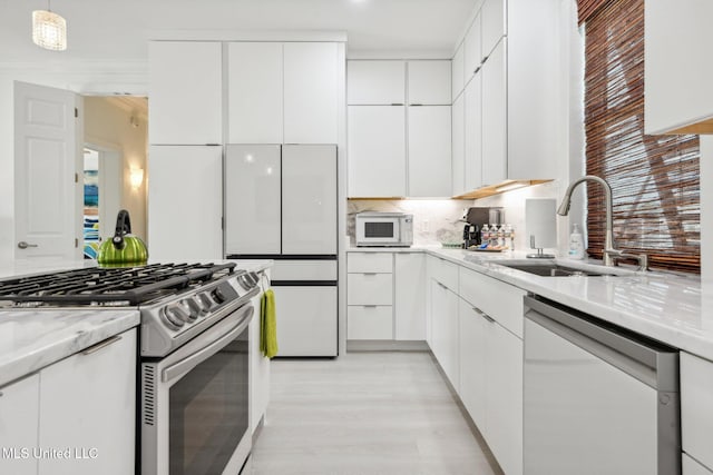 kitchen featuring stainless steel appliances, modern cabinets, a sink, and white cabinetry