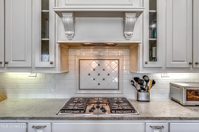 kitchen featuring tasteful backsplash, a toaster, white cabinets, and stainless steel gas stovetop