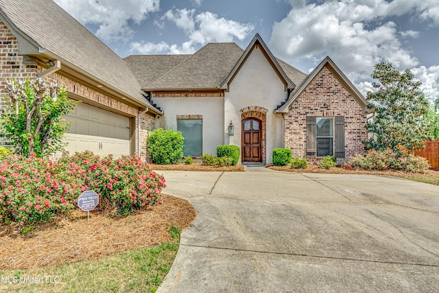 view of front of house featuring a garage, stucco siding, brick siding, a shingled roof, and concrete driveway