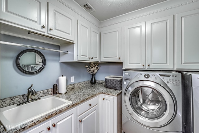laundry room with visible vents, washing machine and dryer, a textured ceiling, a sink, and cabinet space