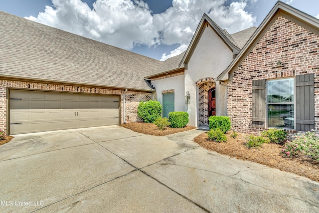 view of front of property featuring roof with shingles, stucco siding, concrete driveway, and brick siding