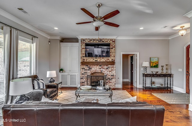 living room featuring a ceiling fan, visible vents, a brick fireplace, wood finished floors, and ornamental molding
