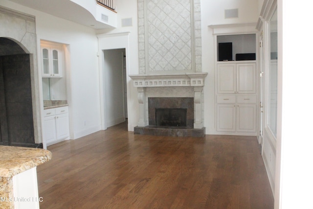 unfurnished living room with a tiled fireplace, dark wood-type flooring, and a high ceiling