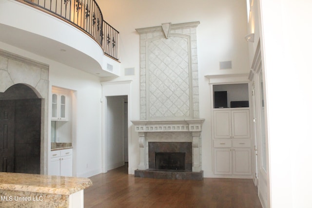 unfurnished living room featuring dark wood-type flooring, a tiled fireplace, and a high ceiling