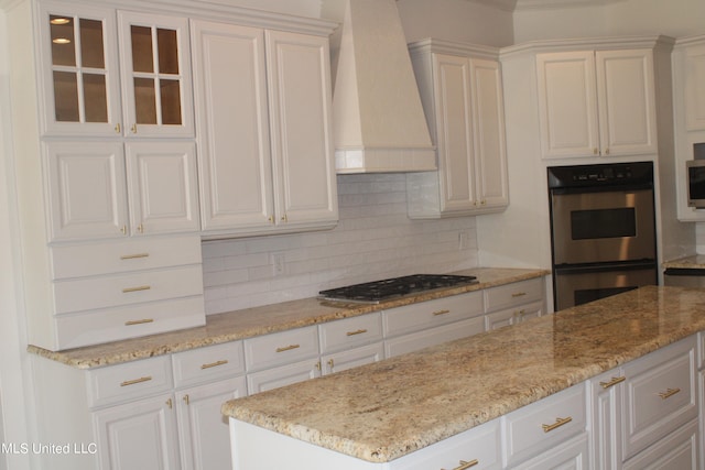 kitchen featuring decorative backsplash, premium range hood, white cabinetry, light stone countertops, and stainless steel appliances