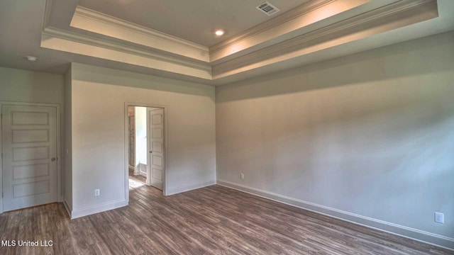 empty room featuring visible vents, a tray ceiling, dark wood-style floors, baseboards, and ornamental molding