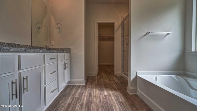 full bathroom featuring vanity, a bath, a stall shower, baseboards, and wood finished floors