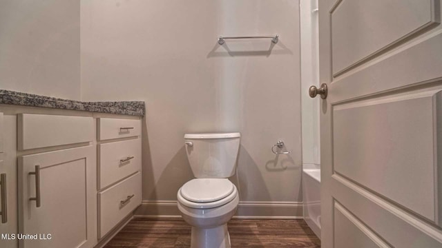 bathroom featuring toilet, a bath, wood finished floors, and baseboards