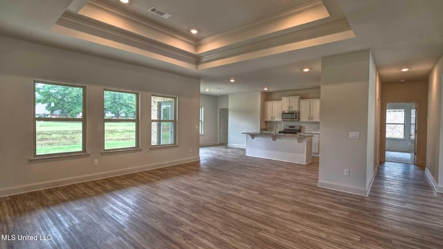 unfurnished living room featuring crown molding, visible vents, a tray ceiling, dark wood-style floors, and baseboards