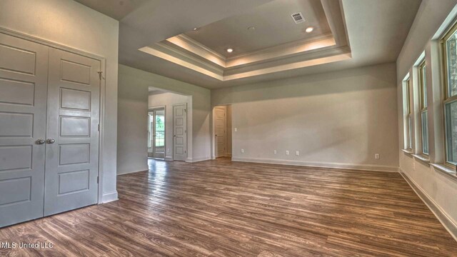 empty room featuring a raised ceiling, visible vents, baseboards, dark wood-style flooring, and ornamental molding
