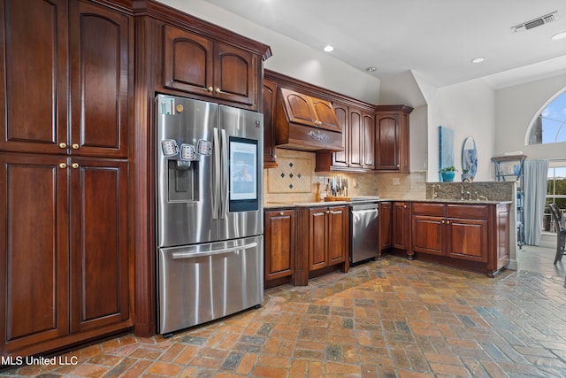 kitchen with kitchen peninsula, appliances with stainless steel finishes, tasteful backsplash, light stone counters, and premium range hood