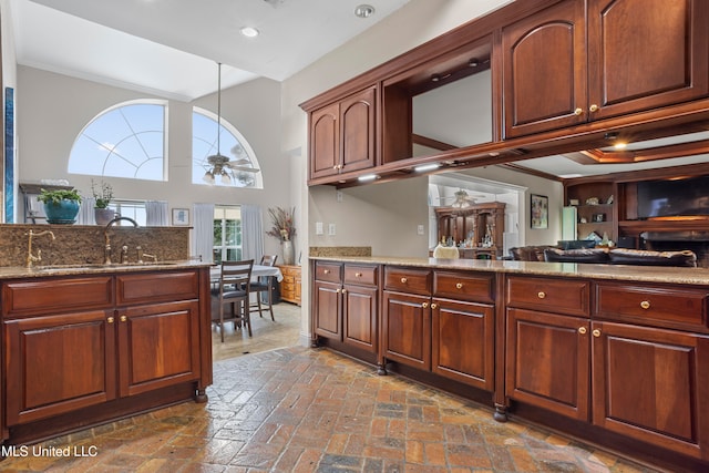 kitchen with ceiling fan, sink, hanging light fixtures, a high ceiling, and light stone counters