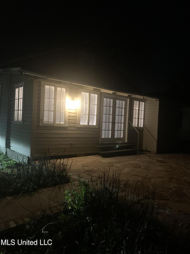 property exterior at night with french doors, entry steps, and a patio area