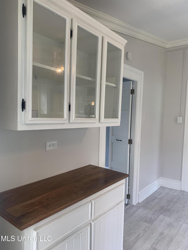 kitchen featuring light wood-type flooring, butcher block counters, crown molding, glass insert cabinets, and baseboards