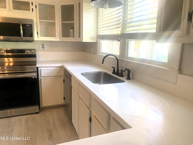 kitchen with glass insert cabinets, light countertops, light wood-style floors, stainless steel appliances, and a sink