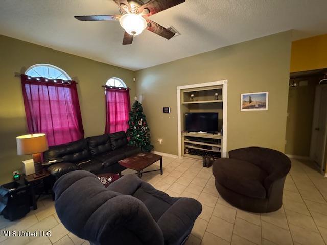 living room featuring light tile patterned floors, built in features, baseboards, ceiling fan, and a textured ceiling