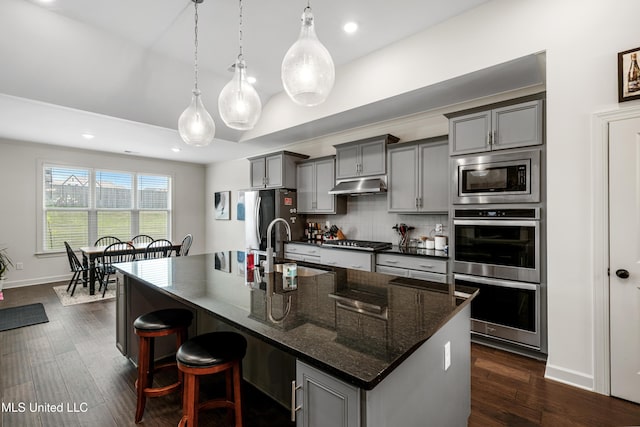 4432 John Wood Ln, Olive Branch, MS 38654 - kitchen featuring appliances with stainless steel finishes, gray cabinetry, under cabinet range hood, a center island with sink, and a kitchen bar