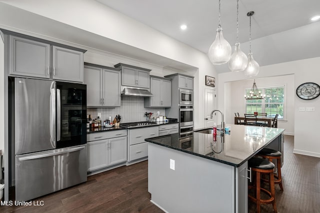 4432 John Wood Ln, Olive Branch, MS 38654 - kitchen featuring appliances with stainless steel finishes, under cabinet range hood, gray cabinetry, dark wood finished floors, and a center island with sink