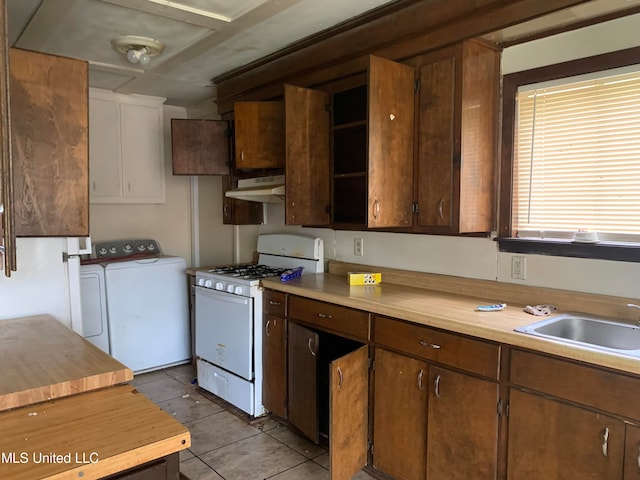 kitchen with light tile patterned floors, white range with gas stovetop, dark brown cabinetry, sink, and washer and clothes dryer