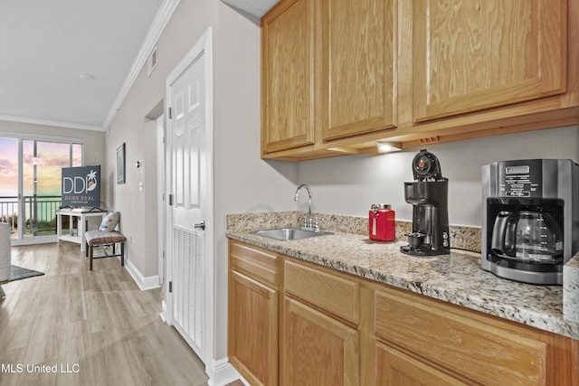 kitchen with crown molding, baseboards, light wood-type flooring, light stone counters, and a sink