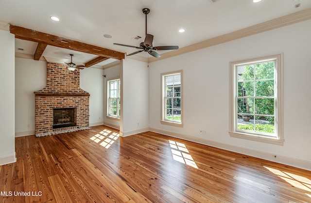 unfurnished living room with wood-type flooring, a wealth of natural light, a brick fireplace, and beamed ceiling