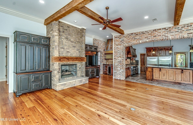 unfurnished living room with beam ceiling, brick wall, light hardwood / wood-style flooring, and a fireplace