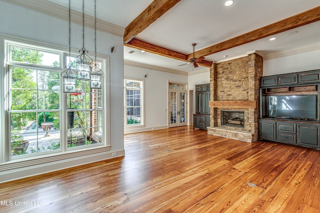 unfurnished living room featuring ceiling fan with notable chandelier, a fireplace, beamed ceiling, crown molding, and hardwood / wood-style flooring