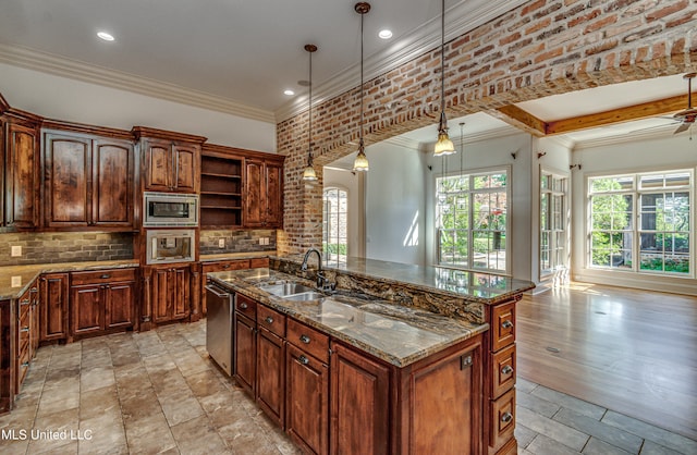 kitchen featuring stainless steel appliances, dark stone counters, a center island with sink, sink, and decorative light fixtures