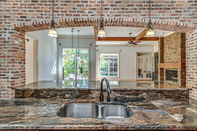 kitchen with dark stone countertops, a fireplace, decorative light fixtures, sink, and brick wall