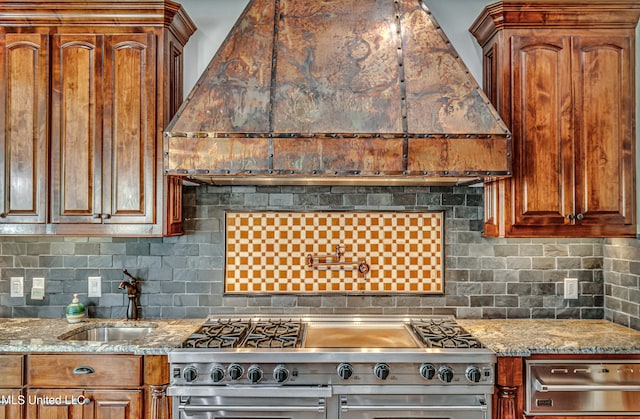 kitchen with light stone countertops, sink, decorative backsplash, and stainless steel range