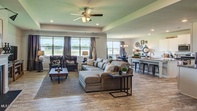 living room with a raised ceiling, sink, light hardwood / wood-style floors, and ceiling fan with notable chandelier