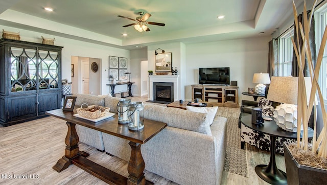 living room featuring a raised ceiling, ceiling fan, and light wood-type flooring