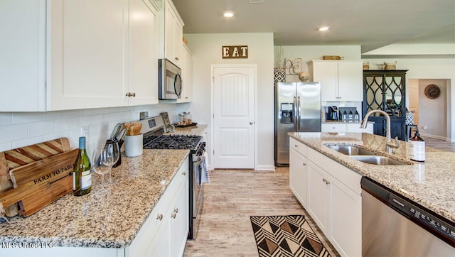 kitchen featuring light stone countertops, sink, stainless steel appliances, white cabinets, and light wood-type flooring