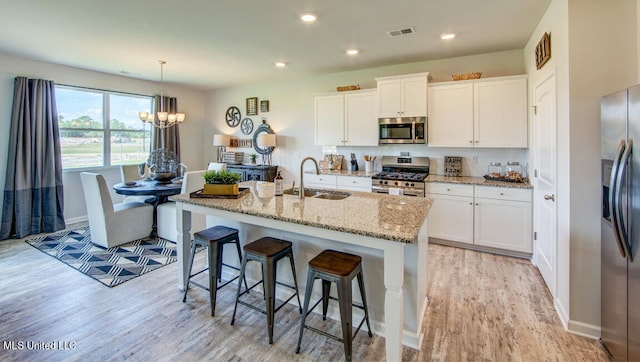 kitchen featuring white cabinetry, sink, stainless steel appliances, a chandelier, and a kitchen island with sink