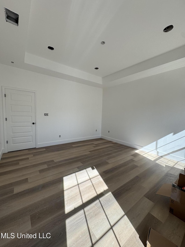 spare room featuring a tray ceiling and dark wood-type flooring