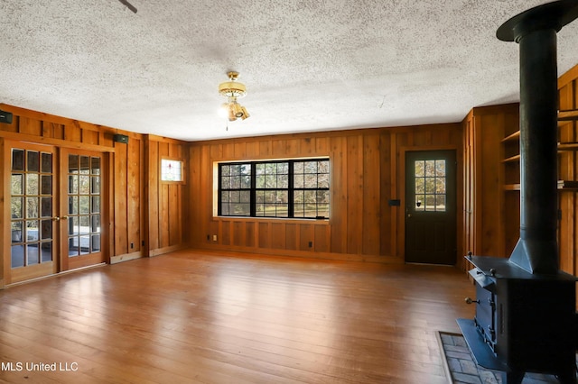 unfurnished living room featuring a healthy amount of sunlight, wood-type flooring, french doors, and a wood stove