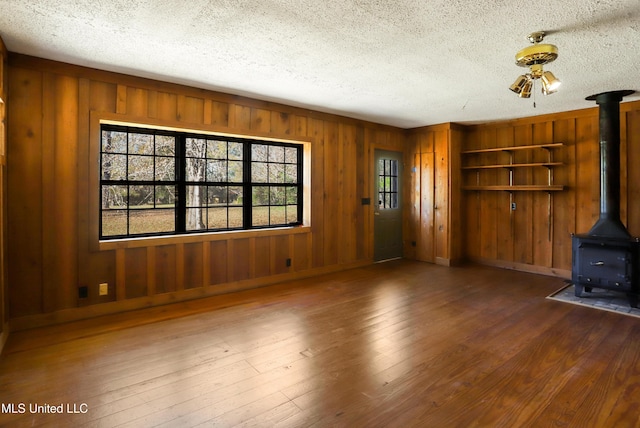 unfurnished living room featuring a textured ceiling, dark wood-type flooring, and a wood stove