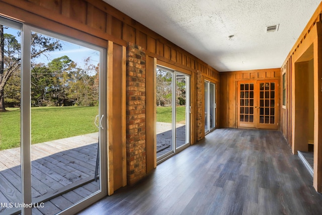 doorway to outside with a textured ceiling, dark hardwood / wood-style floors, french doors, and wooden walls