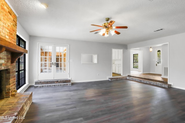 unfurnished living room featuring ceiling fan, dark wood-type flooring, a fireplace, french doors, and a textured ceiling