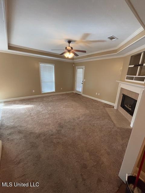 unfurnished living room with ceiling fan, carpet floors, crown molding, a tray ceiling, and a tiled fireplace