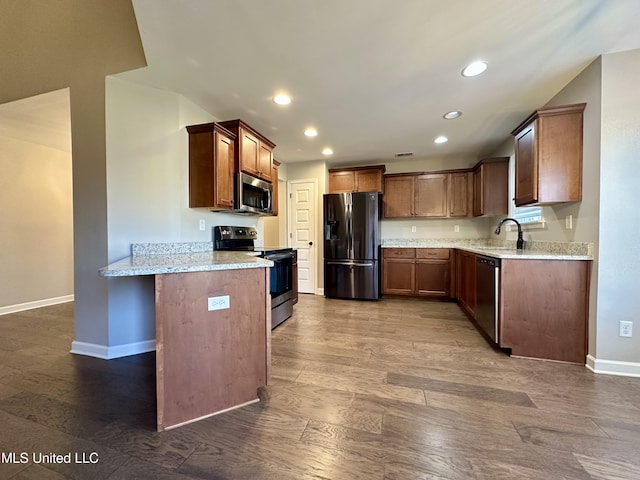 kitchen with sink, hardwood / wood-style flooring, light stone counters, kitchen peninsula, and stainless steel appliances