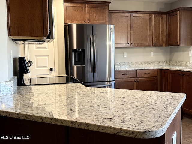 kitchen featuring stainless steel fridge, black range, and light stone counters