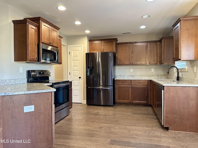 kitchen with light stone counters, sink, stainless steel appliances, and light hardwood / wood-style floors