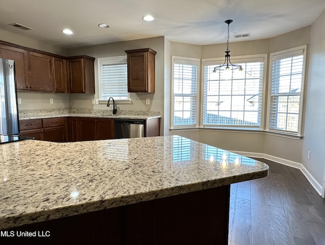 kitchen with appliances with stainless steel finishes, dark hardwood / wood-style flooring, light stone counters, and hanging light fixtures