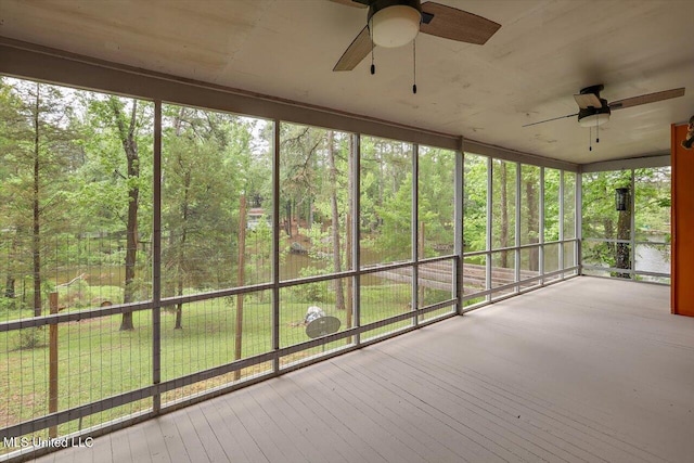 unfurnished sunroom with ceiling fan and a forest view